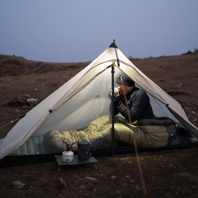 A man in a sleeping bag sitting in a tent looking at the camera outdoors at night