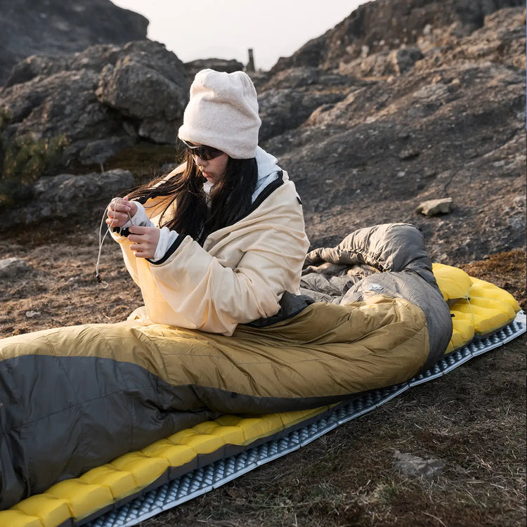A girl in a sleeping bag lying on a sleeping mat resting in a tent outdoors