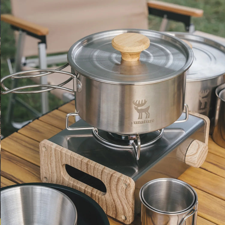 A person pours water from a kettle into a cup on a folding camping table outdoors.