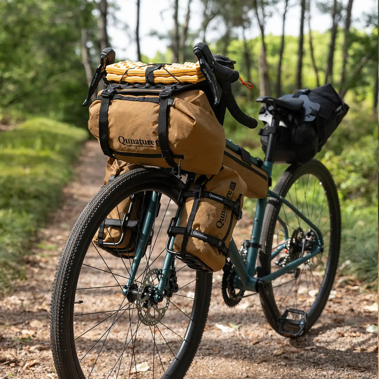 A man is riding a bicycle outdoors with a loaded khaki frame bag