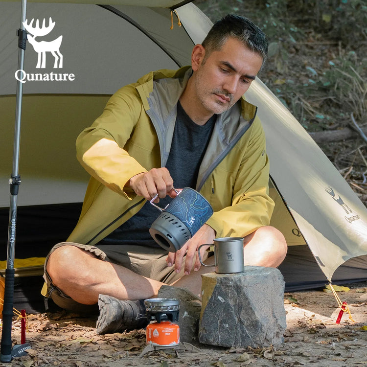 A man sitting outdoors in a tent pouring water from one cup into another