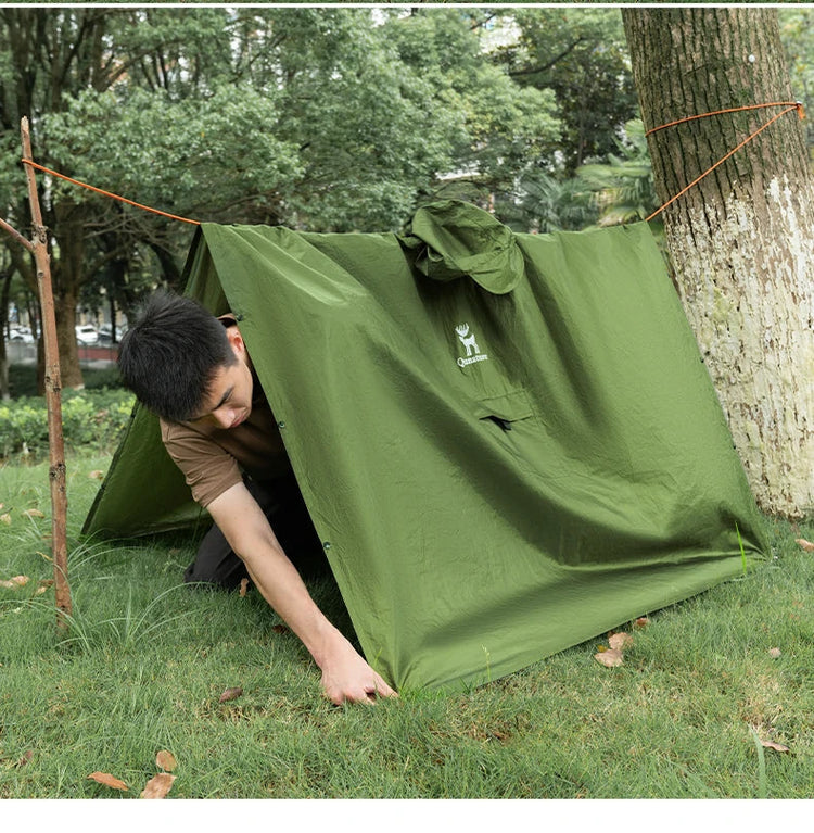 A boy is putting on a raincoat outdoors on the grass