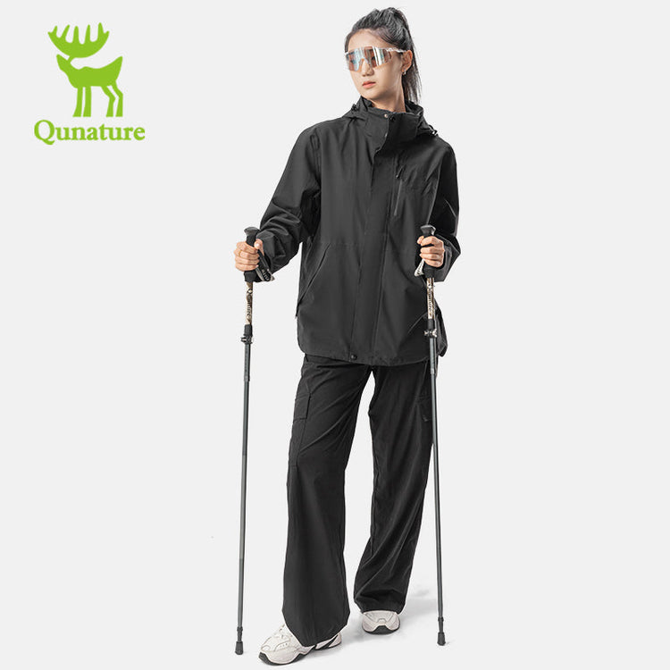 A woman in black stands with a trekking pole in each hand
