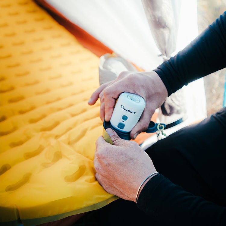 A person is inflating a yellow sleeping mat with a mini electric air pump