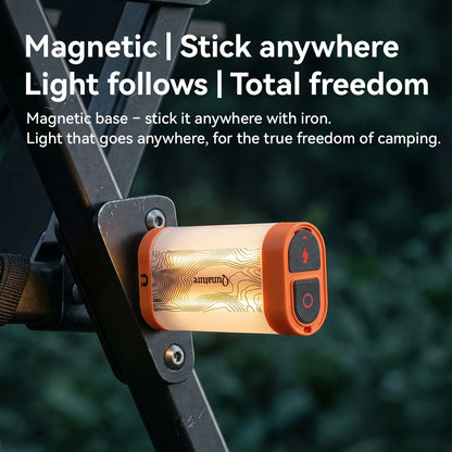 A small cylindrical camping light with an orange end cap and glowing warm-white body, mounted on a black metal frame outdoors. Large text at the top reads 'Magnetic | Stick anywhere | Light follows | Total freedom' with a smaller explanatory subtitle.
