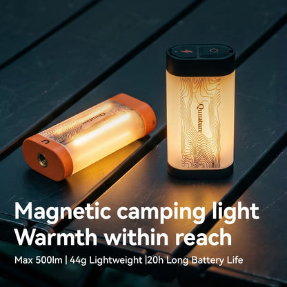 Two Qunature magnetic camping lights on a dark wooden surface, one standing upright and one lying on its side, both glowing with a warm light. White text at the bottom reads 'Magnetic camping light Warmth within reach Max 500lm | 44g Lightweight | 20h Long Battery Life'.