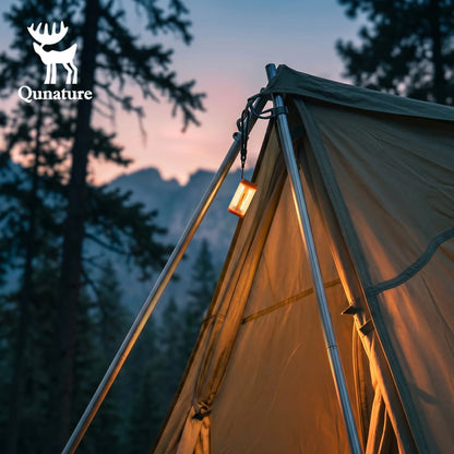 A Qunature brand tent pitched outdoors in a forest at dusk, with a warm lantern hanging from the peak and mountains visible in the background.