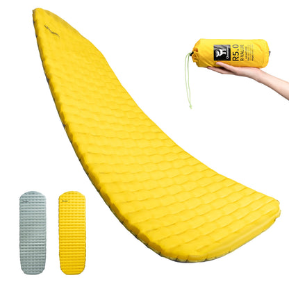 Yellow inflatable sleeping pad with rolled-up pad and hand holding it on a white background