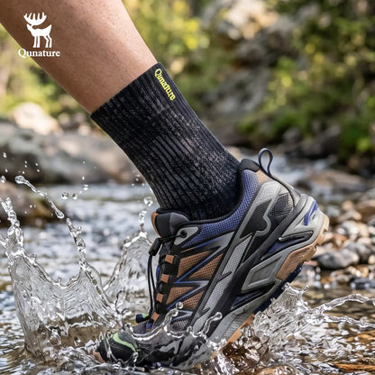 A person's foot wearing a black Qunature athletic sock and a gray, black, and blue water-resistant hiking shoe, splashing through a shallow stream outdoors. The Qunature brand logo is visible on the sock and as an overlay in the top left corner.
