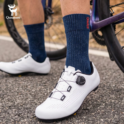 A close-up of a cyclist's lower legs wearing white cycling shoes with dial closures and navy blue crew socks, standing on asphalt next to a purple bicycle. The Qunature brand logo is visible in the top left corner.