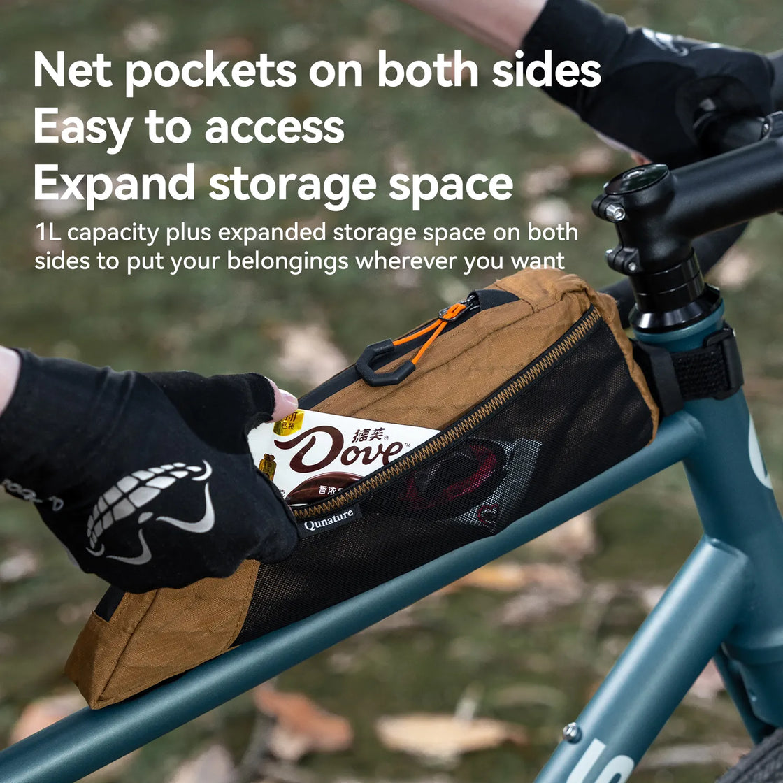 A khaki top tube bike bag with many storage pockets is mounted on a bicycle outdoors, and someone is taking something out