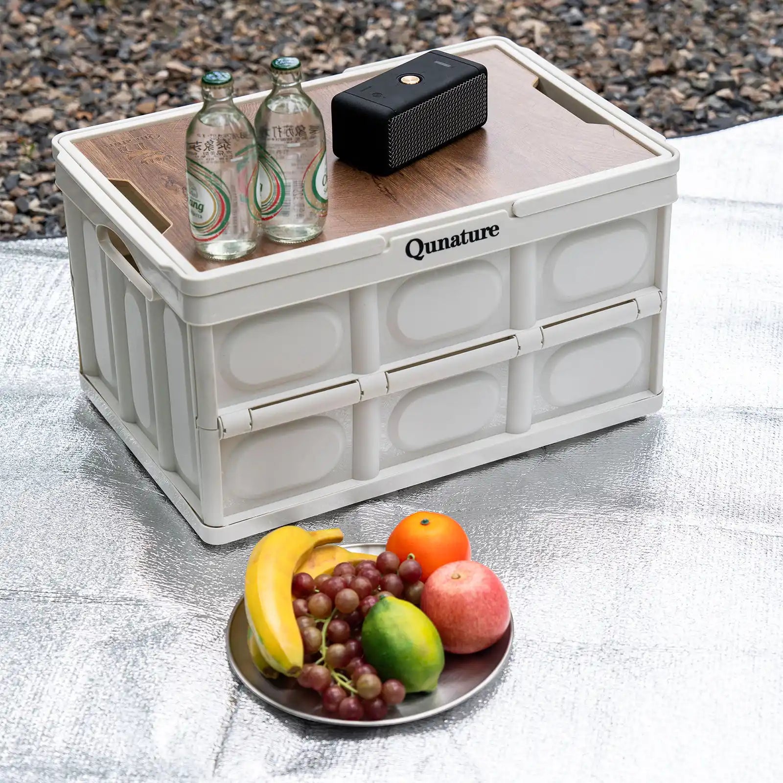 White Qunature storage crate with bottles, a speaker, and fruits on a textured surface.