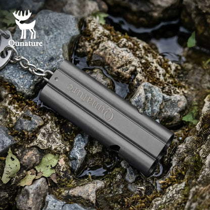 A dark gray metallic keychain tool with embossed 'Ounature' branding, resting on wet rocks outdoors. A key ring and chain are attached on the left, and the Ounature logo watermark appears in the top-left corner.