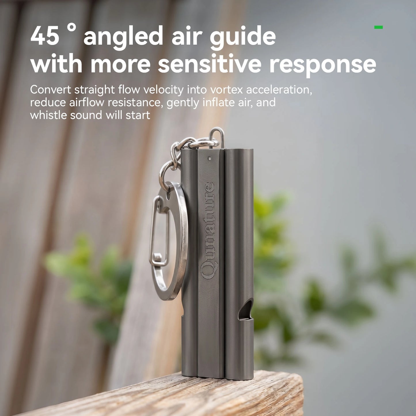 A metallic gray and silver Breathe Air whistle with a keychain ring, standing upright on a wooden surface with a blurred outdoor background. White text at the top reads '45° angled air guide with more sensitive response'.