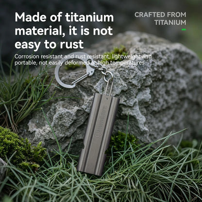 A titanium keychain battery holder with a metallic silver-gray finish, shown resting on green grass and a gray rock outdoors. White text overlays on the left describe its rust-resistant titanium material, and text on the top right reads 'CRAFTED FROM TITANIUM'.