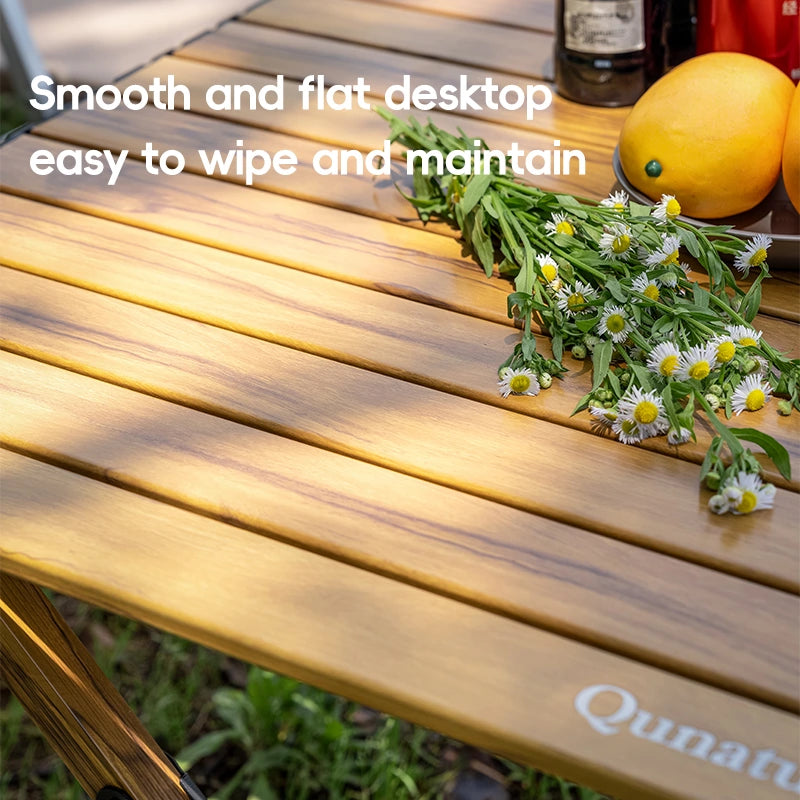 Wooden table with flowers and text 'Smooth and flat desktop easy to wipe and maintain' on a blurred natural background