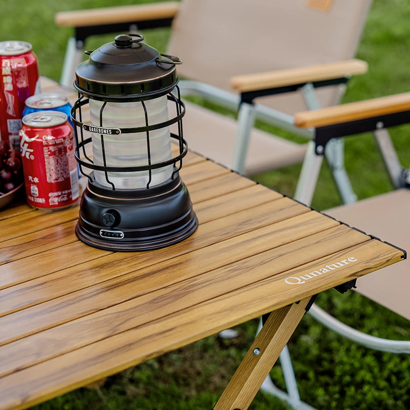 Black lantern on a wooden camping table with Coca-Cola cans in the background