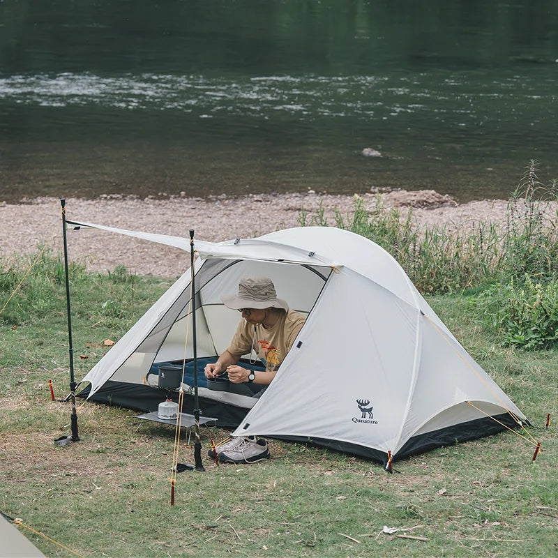 Person sitting inside a white tent by a river
