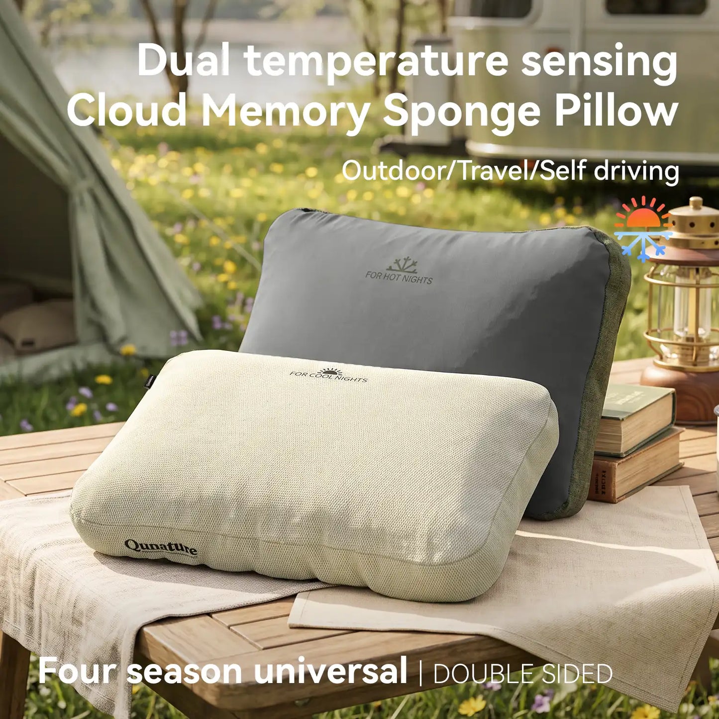 Two Qunature memory foam pillows displayed outdoors on a wooden table, with one in light beige in front and one in dark gray behind. The background shows a blurred camping scene with a tent, grass, and flowers.