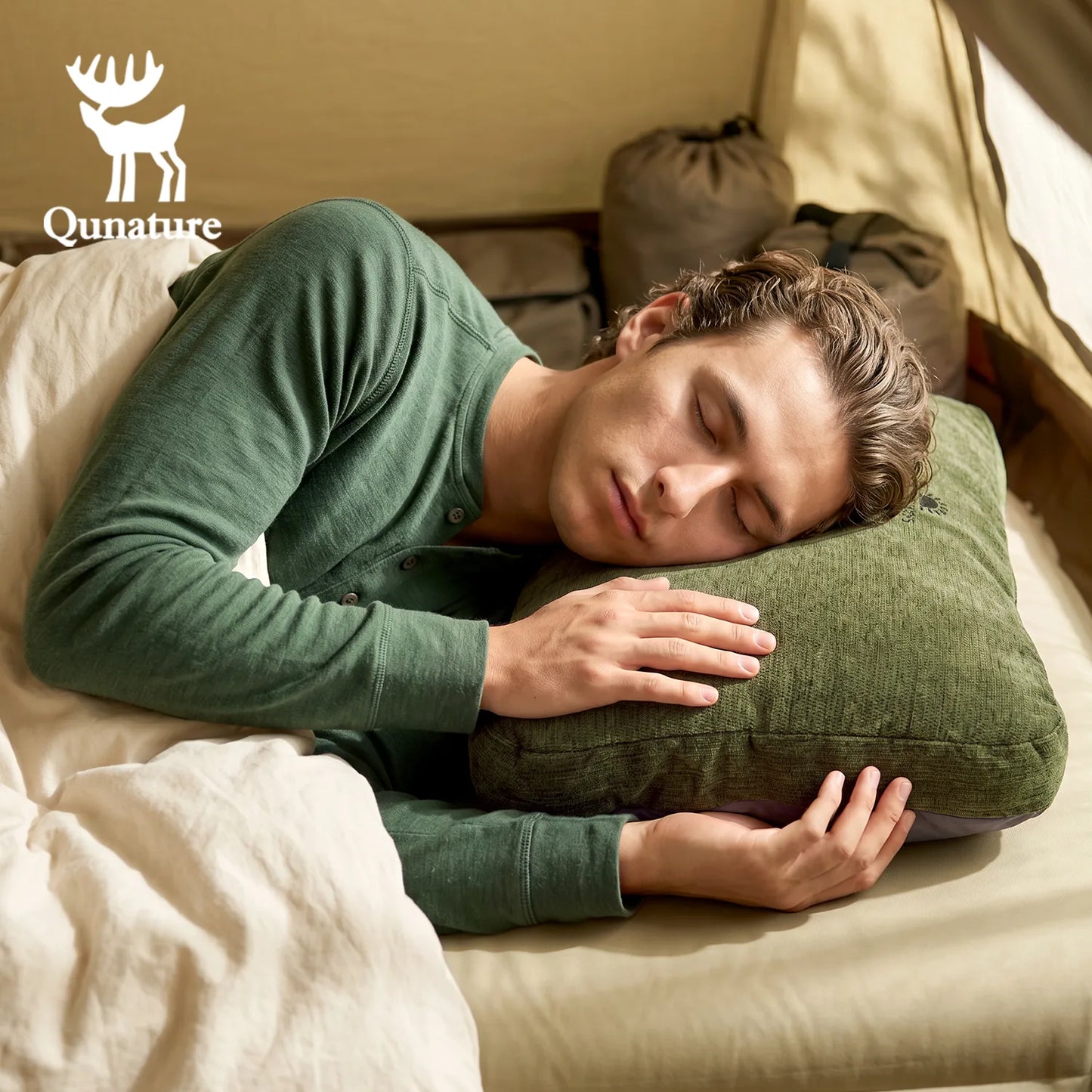 A man sleeping soundly in bed, resting his head on an olive green Qunature pillow. He is wearing a matching green long-sleeve henley shirt.