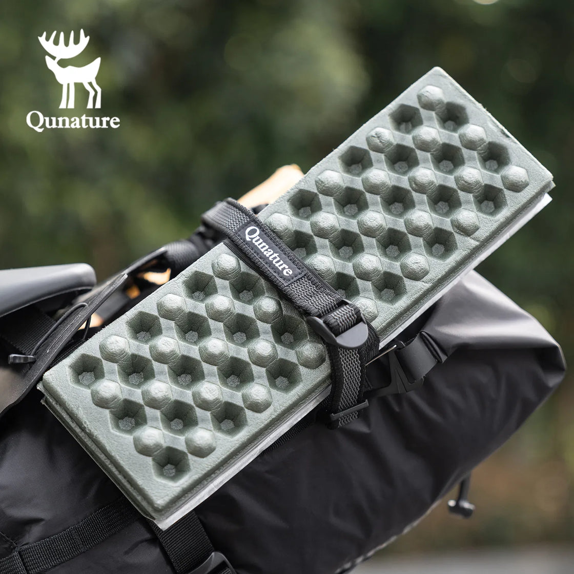 A black multi-purpose cargo binding belt is used to tie a green object to the bag.