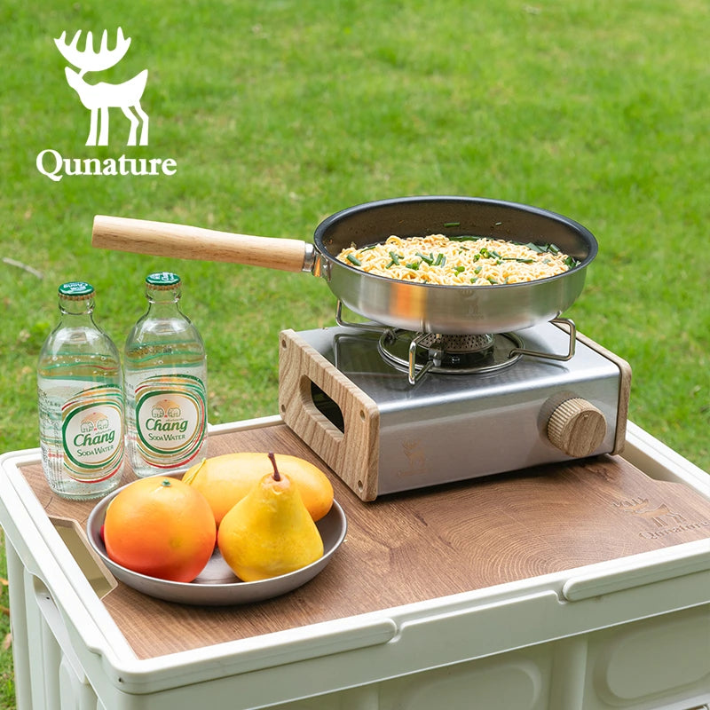 Portable stove with a frying pan on a wooden table outdoors, featuring Qunature branding.