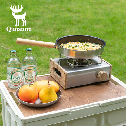 Portable stove with a frying pan on a wooden table outdoors, featuring Qunature branding.