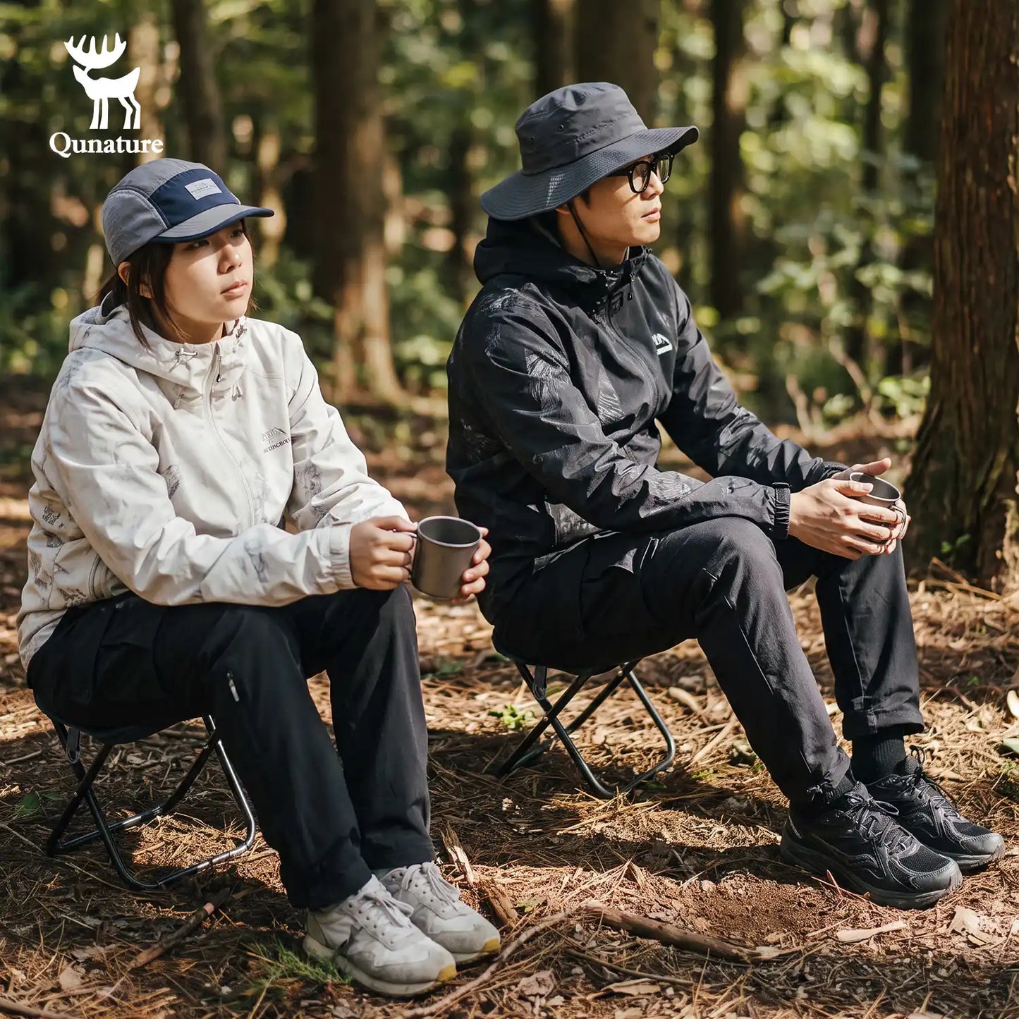Two people sitting on folding camp chairs in a forest, wearing outdoor jackets and holding mugs. The Qunature brand logo is visible in the top left corner.