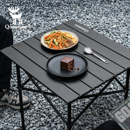 Black folding table with food on a gravel surface, featuring the Qunature brand.