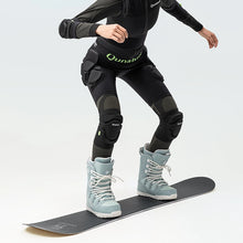 A person standing on a snowboard wearing a pair of black protective knee pads with thick sponge