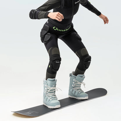 A person standing on a snowboard wearing a pair of black protective knee pads with thick sponge