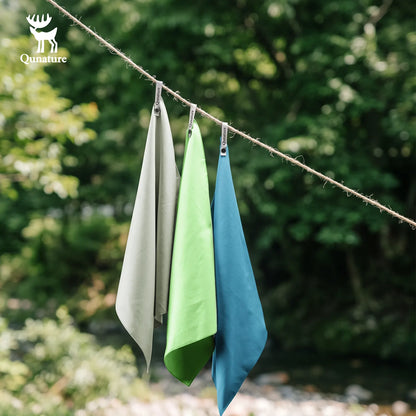 Three fabric cloths in beige, green, and blue hang from a rope outdoors with a blurred forest background. A Qunature logo is visible in the top-left corner.