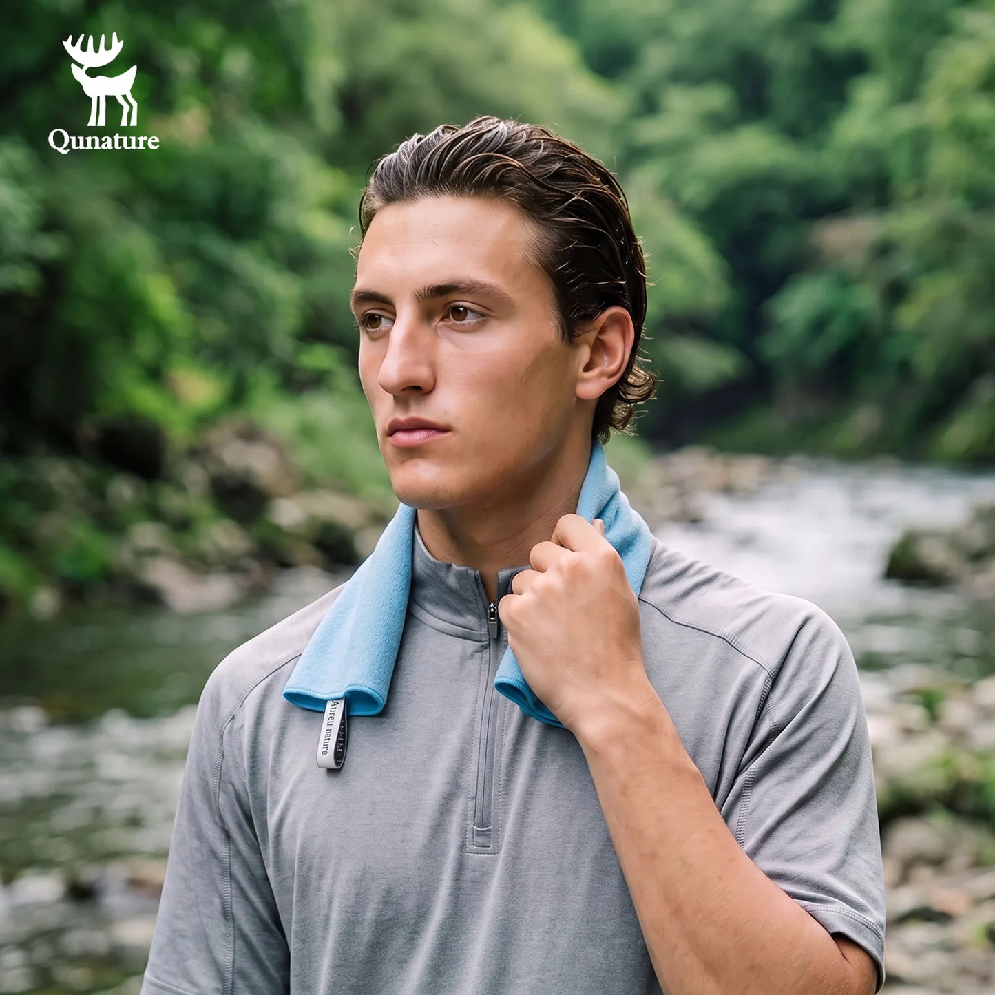 A man outdoors by a river wearing a gray quarter-zip athletic shirt with a light blue neck gaiter. The Qunature brand logo is visible in the top left corner.