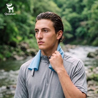 A man outdoors by a river wearing a gray quarter-zip athletic shirt with a light blue neck gaiter. The Qunature brand logo is visible in the top left corner.