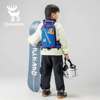 A little boy is wearing a ski training strap with storage pockets and carrying a snow helmet and skis