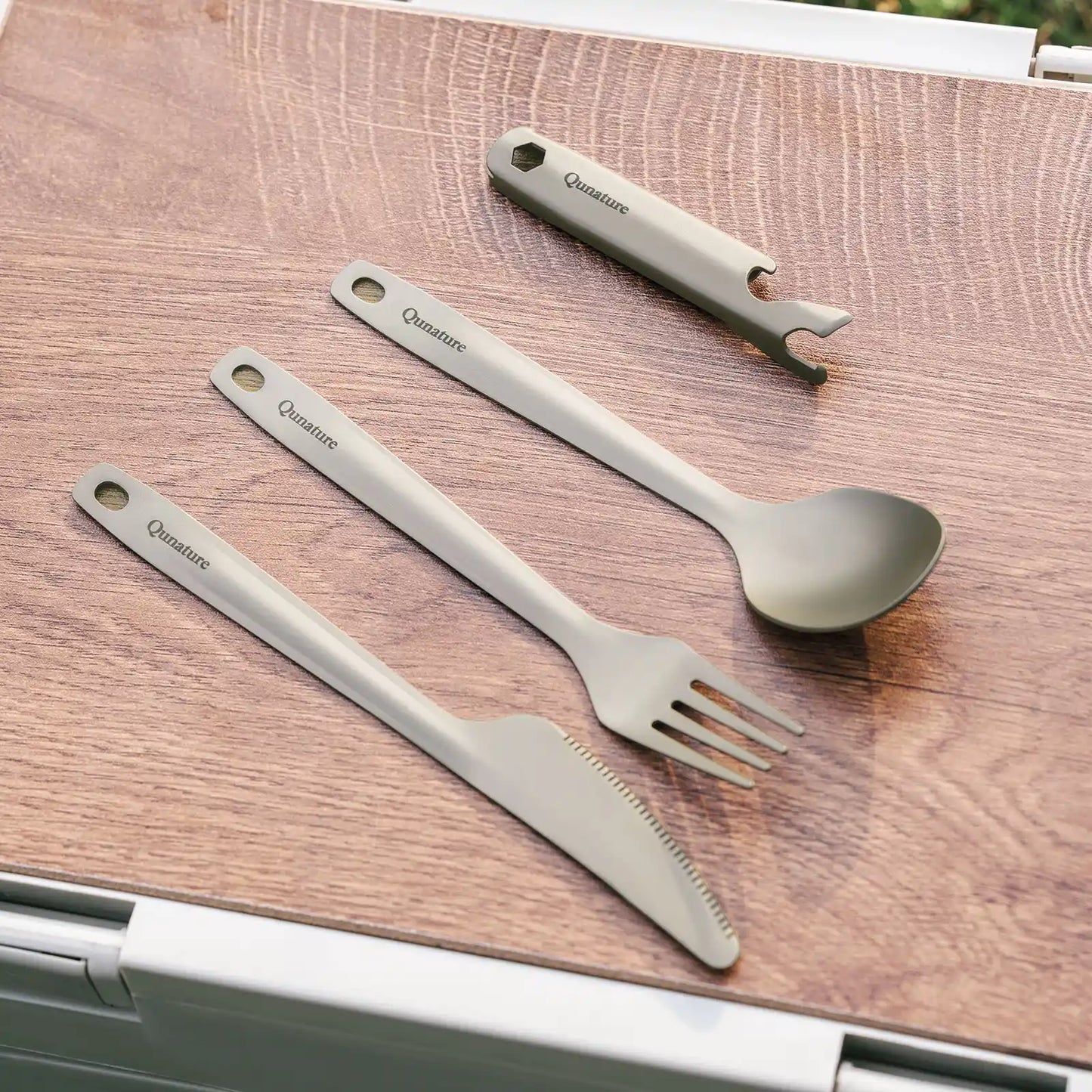 Set of stainless steel utensils including a fork, knife, spoon, and bottle opener on a wooden surface.
