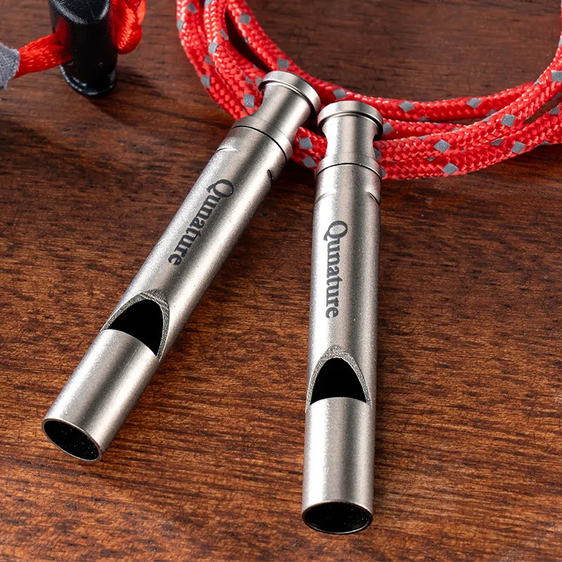 Two metal whistles with a red rope on a wooden surface