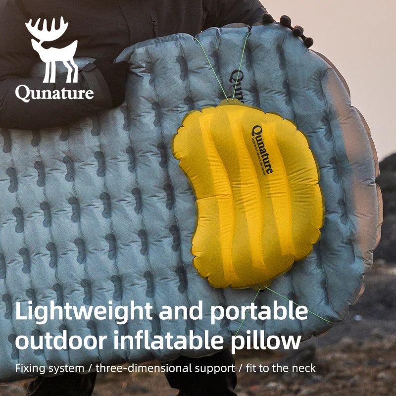 A person is outdoors holding a sleeping pad with a down yellow inflatable ultra-light waterproof camping pillow hanging on it
