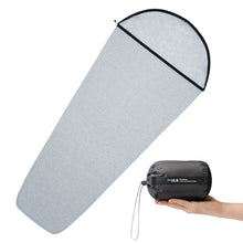 Gray sleeping bag with black zipper and a hand holding a black compression sack labeled 'ULS'.