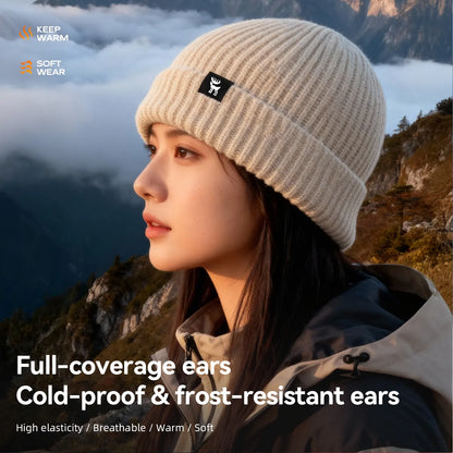 Person wearing a beige knit beanie in a mountainous landscape with promotional text about the product's features.