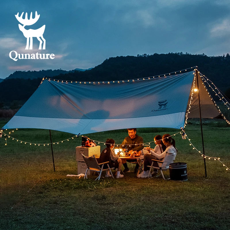 People camping under a Qunature tent with string lights in a scenic outdoor setting.