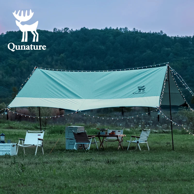Outdoor setting with a Qunature tent, table, and chairs in a grassy field with trees in the background.