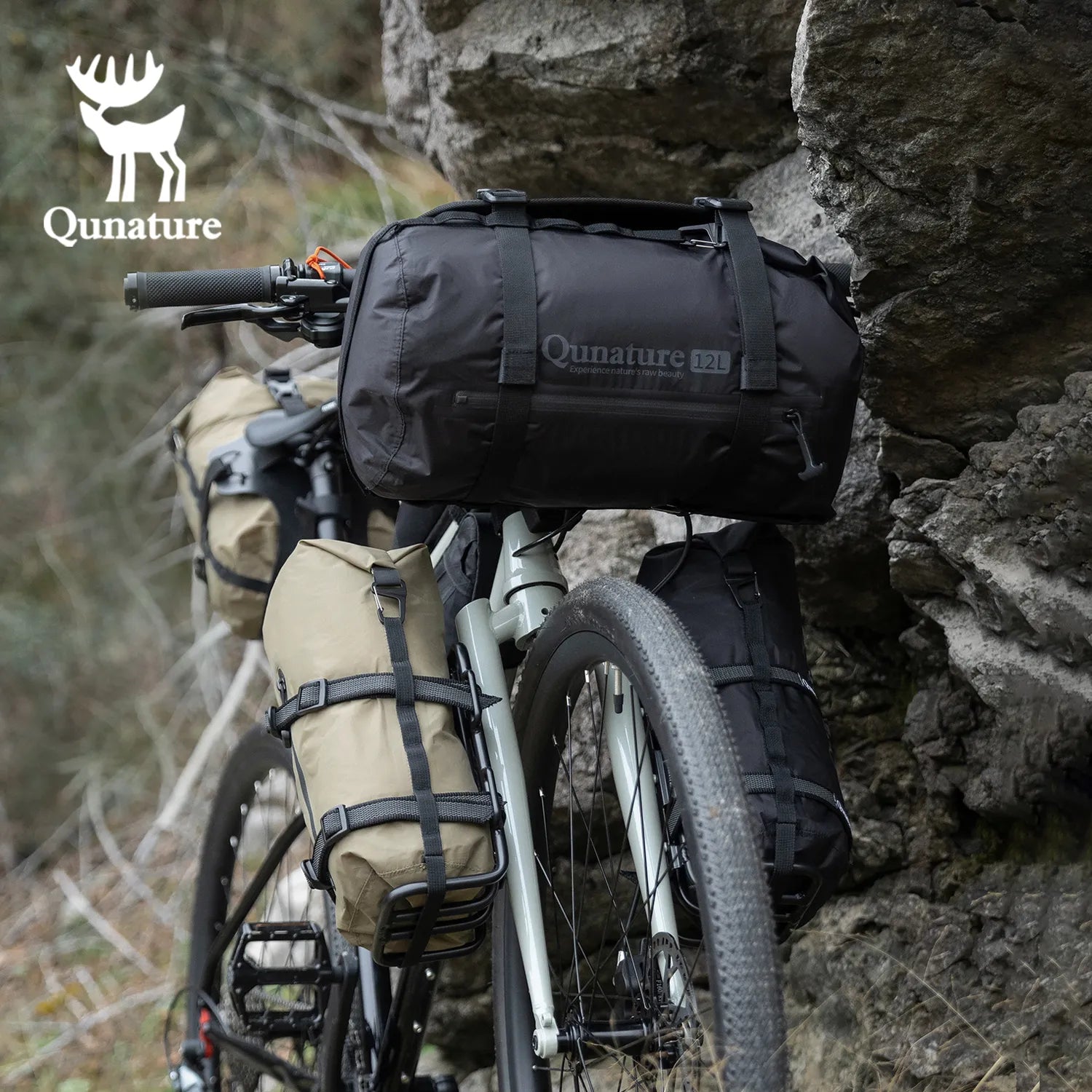 A black 12L large capacity waterproof compression bag is strapped to a gray bicycle next to the mountain