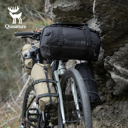 A black 12L large capacity waterproof compression bag is strapped to a gray bicycle next to the mountain