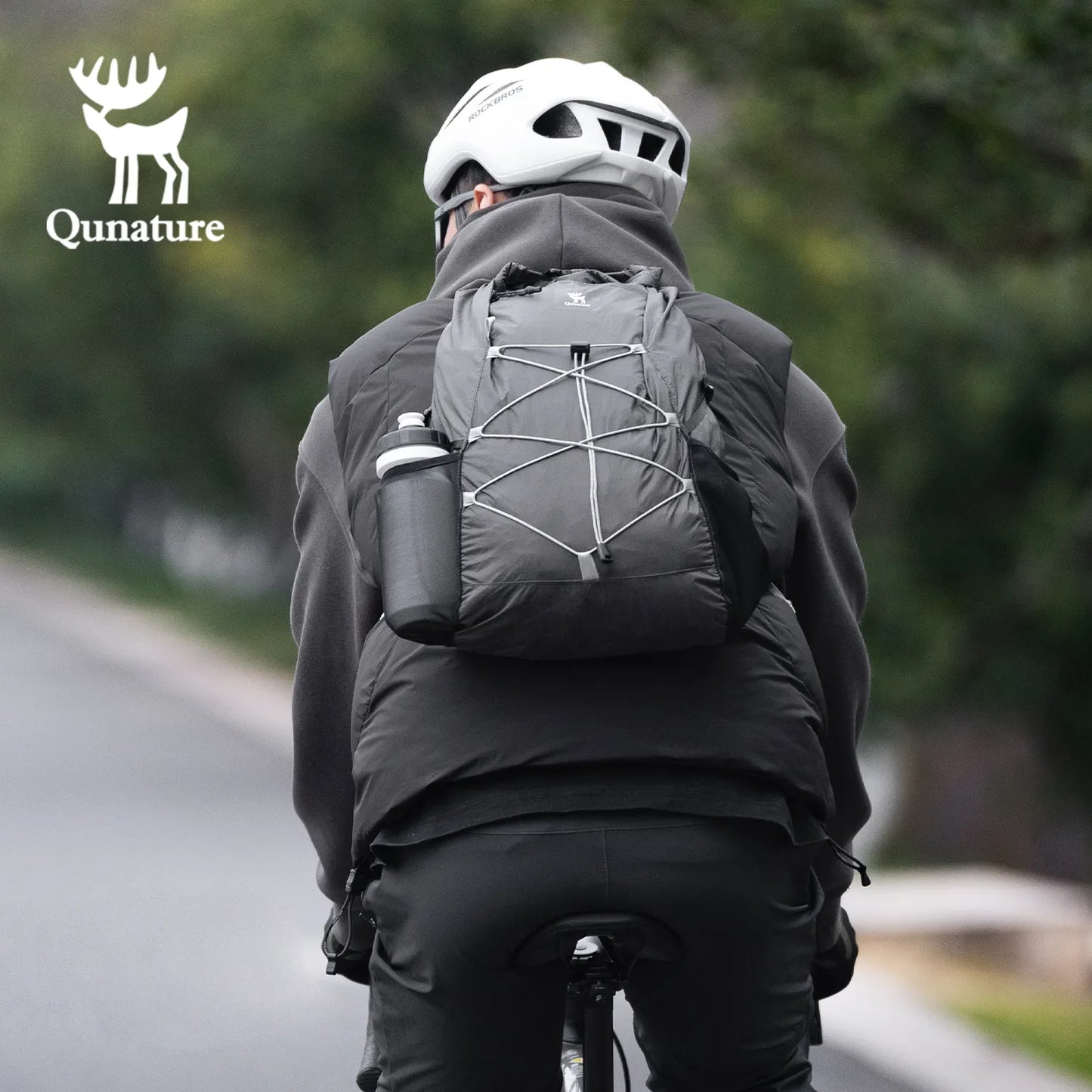 Person wearing a black jacket and helmet with a Black backpack, riding a bike on a road.
