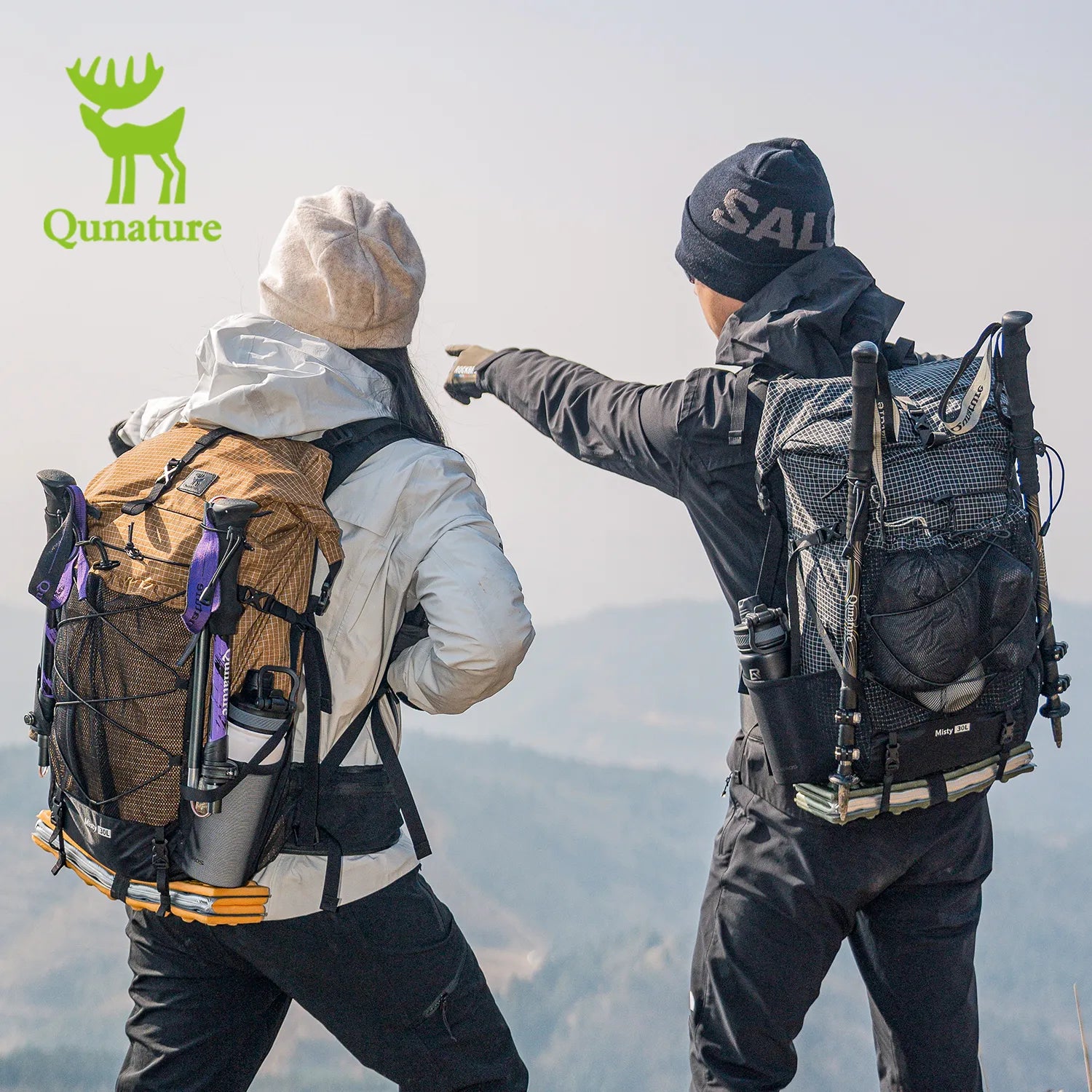 A girl with a khaki waterproof backpack and a boy with a black waterproof backpack on the top of a mountain