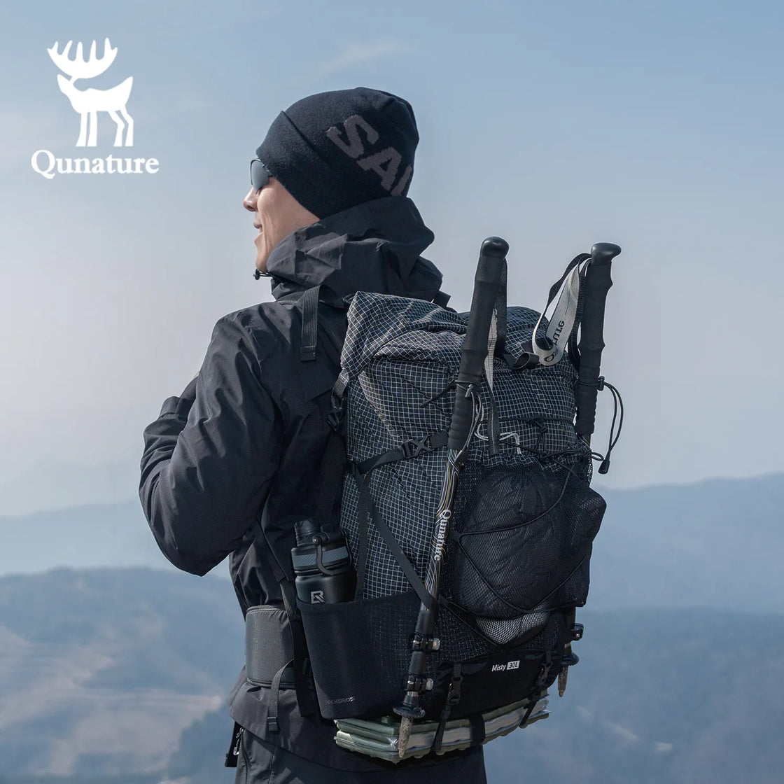 A man wearing a hat and sunglasses and carrying a black backpack is looking into the distance on the mountain