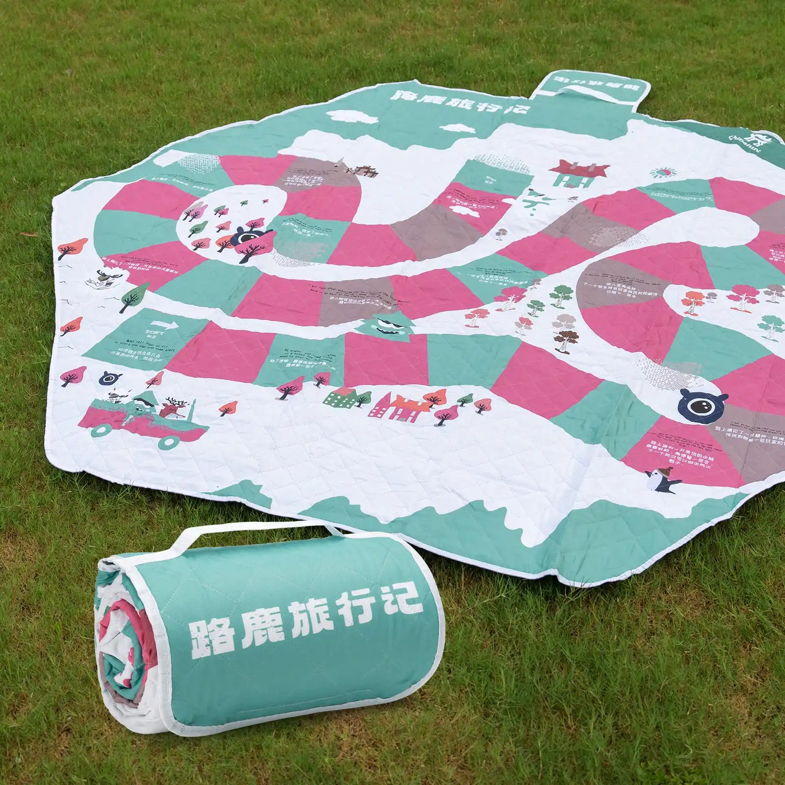 A Qunature branded outdoor picnic mat with a patterned design featuring elements like mountains, trees, and camping gear, in green, beige, and other colors.