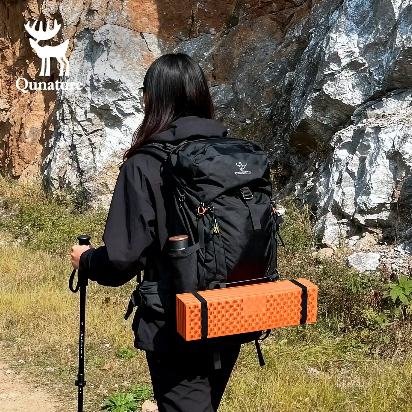 Person hiking with a black backpack and orange box, Qunature logo visible